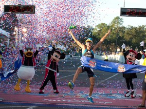 A imagem mostra uma pessoa comemorando por ter terminado a maratona da Disney, ao lado do Mickey, da Minnie e do Donald vestidos com roupas esportivas.