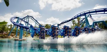 Foto da montanha-russa Manta, do SeaWorld, que mostra o carrinho de ponta-cabeça e entrando na água, com alguns trilhos pintados de azul ao fundo.