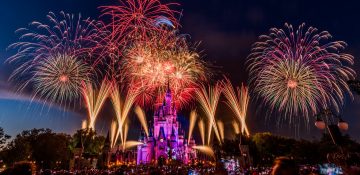 Foto do show de fogos de 4 de julho no Magic Kingdom, com o castelo iluminado em roxo e vermelho.