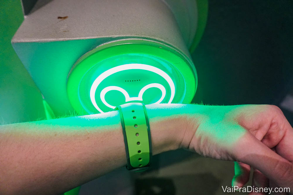 Foto de uma mão com uma MagicBand verdesendo escaneada em uma atração da Disney, no totem de Mickey que fica verde para autorizar a entrada