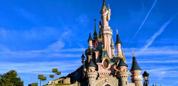 Foto do castelo da Bela Adormecida, na Disneyland de Paris, com o céu azul ao fundo.