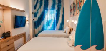 Foto do quarto do Endless Summer, um dos hotéis da Universal, com 2 camas de casal, paredes com uma decoração azul e branca e uma prancha de surf decorativa também azul e branca.