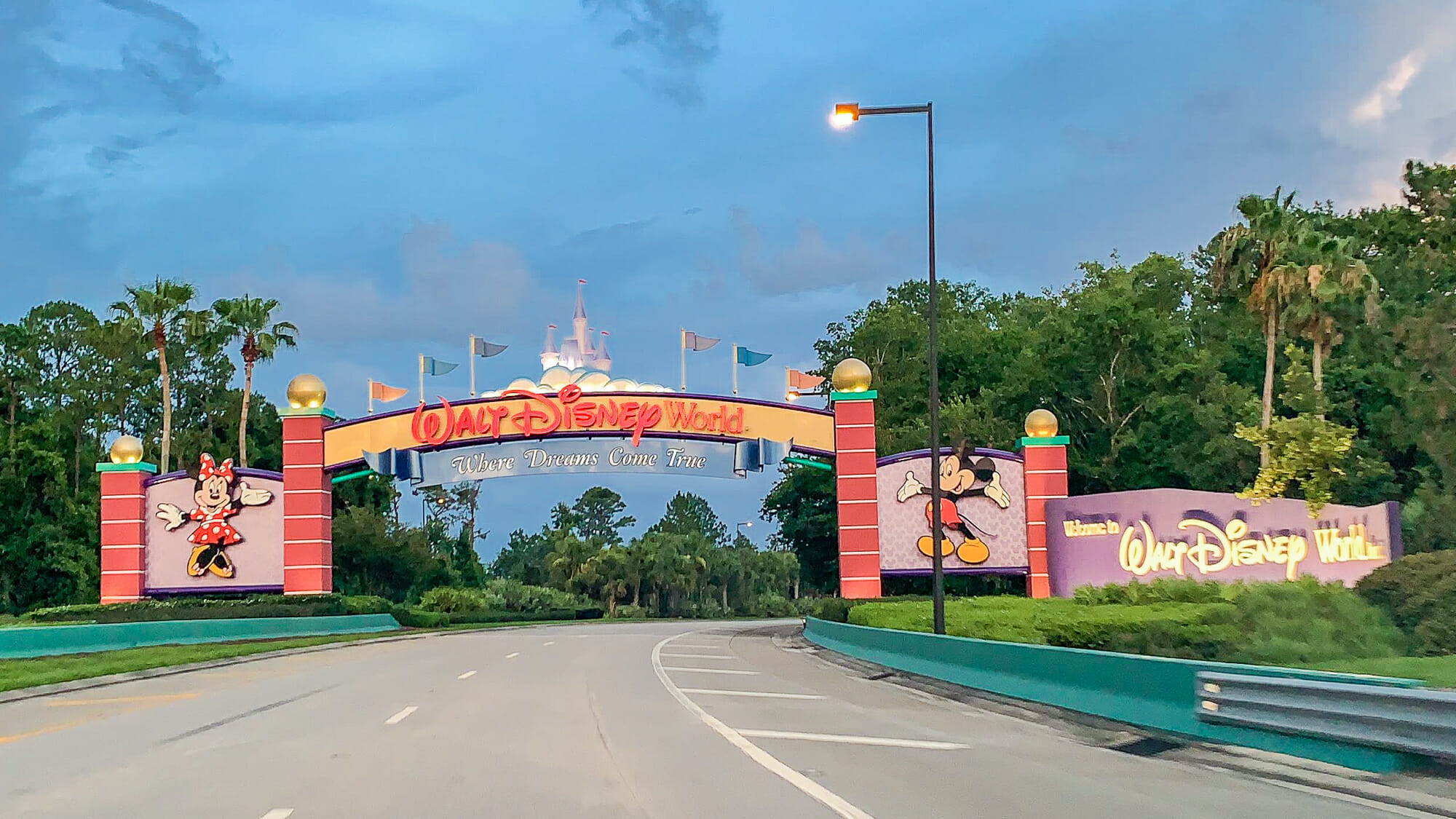 Foto do portal de entrada do complexo da Disney, que tem a Minnie e o Mickey de cada lado, com o céu azul ao fundo.