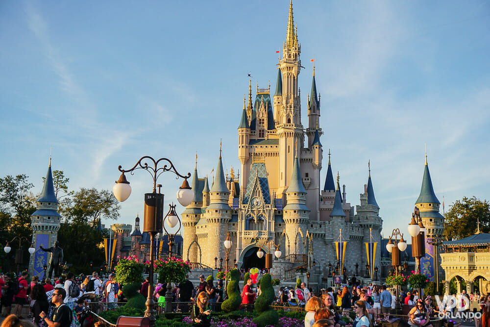 Imagem do Magic Kingdom durante o dia, com muitos visitantes e o Castelo da Cinderela ao fundo.