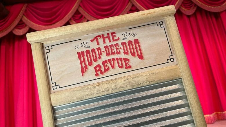 Pôster com o nome do show Hoop-Dee-Doo Revue escrito em madeira, num fundo com cortinas vermelhas de teatro.