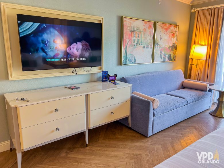 visão da televisão e do sofá do grand floridian. a tv está passando a pequena sereia e há dois quadros de mary poppins ao lado.